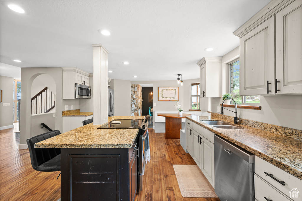 Kitchen featuring light stone counters, appliances with stainless steel finishes, sink, light hardwood / wood-style floors, and white cabinetry