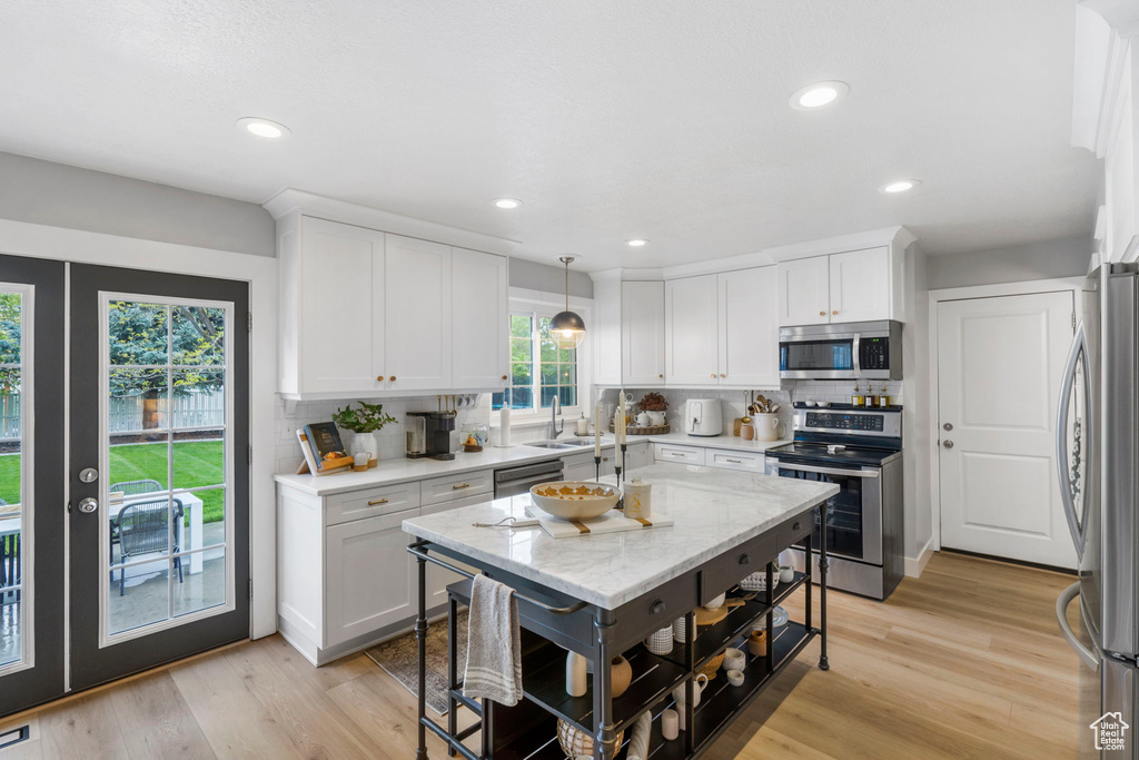 Kitchen with tasteful backsplash, appliances with stainless steel finishes, light hardwood / wood-style flooring, and hanging light fixtures