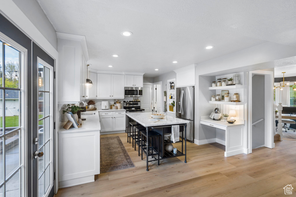 Kitchen featuring light hardwood / wood-style floors, stainless steel appliances, white cabinetry, and hanging light fixtures