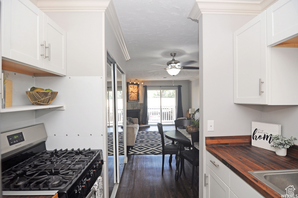 Kitchen with dark wood-type flooring, gas range oven, ornamental molding, butcher block counters, and ceiling fan