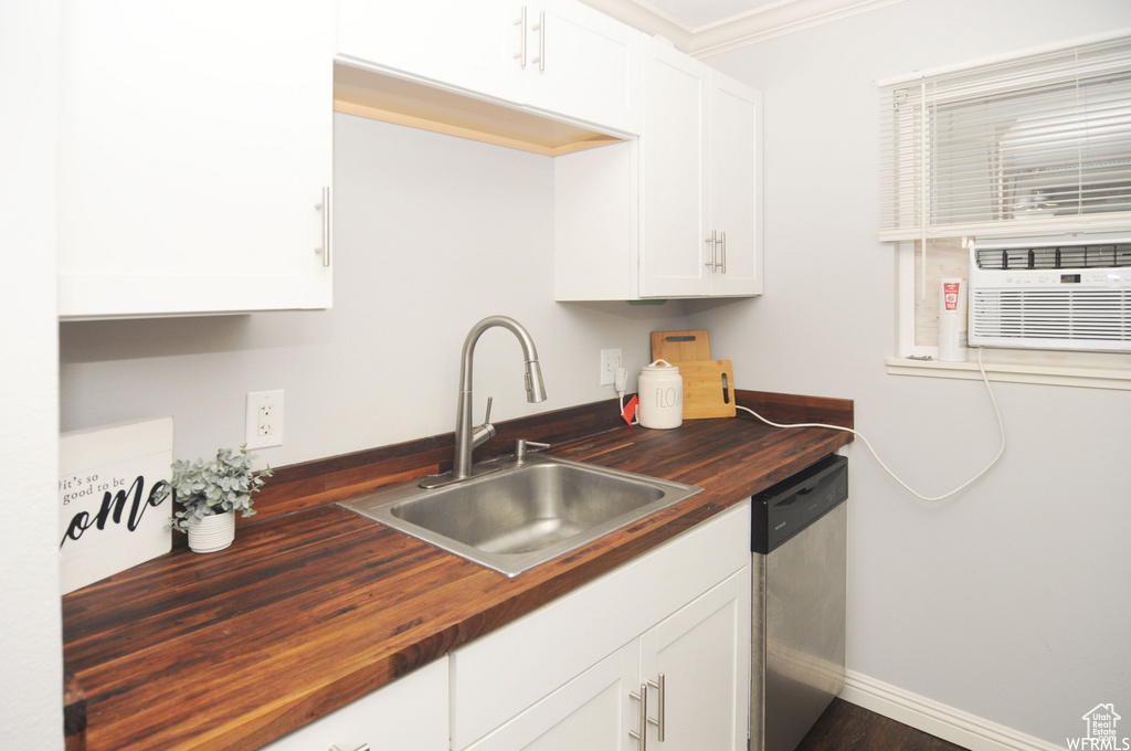 Kitchen with white cabinets, wood counters, crown molding, stainless steel dishwasher, and sink