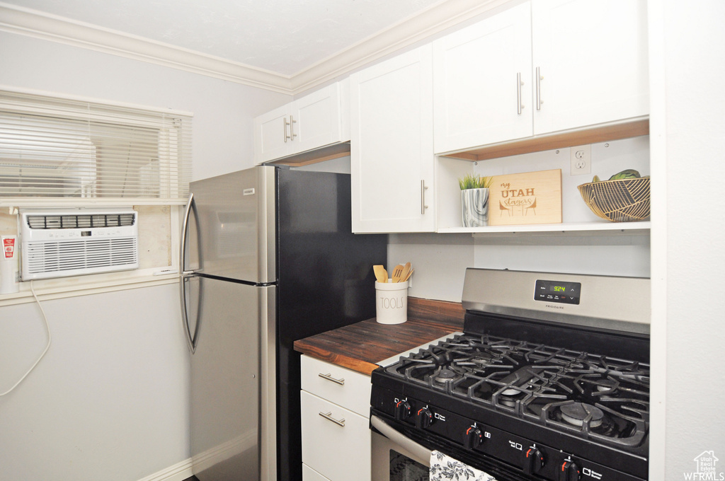 Kitchen featuring gas range, butcher block countertops, white cabinetry, stainless steel fridge, and ornamental molding