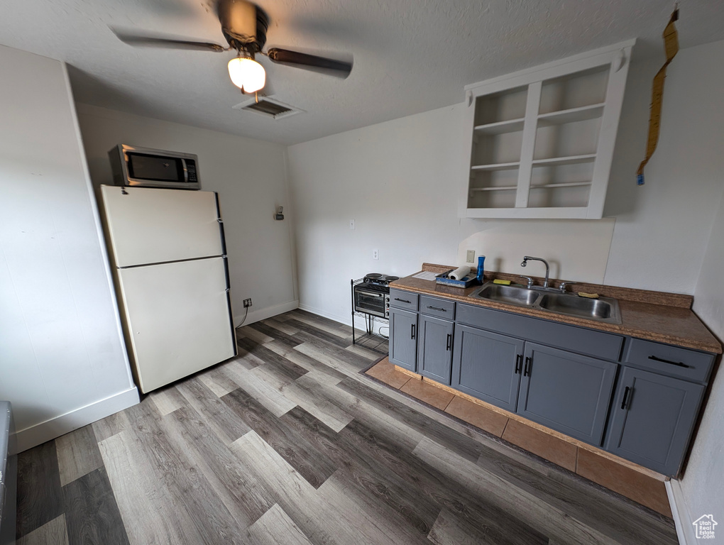 Kitchen with ceiling fan, white refrigerator, sink, hardwood / wood-style flooring, and blue cabinets