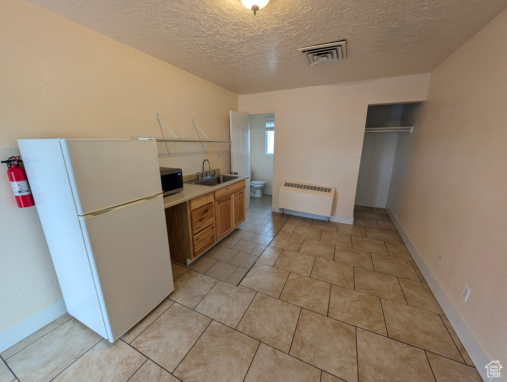 Kitchen with radiator heating unit, light tile floors, white fridge, a textured ceiling, and sink