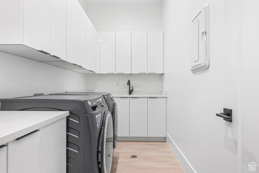 Clothes washing area featuring washer and clothes dryer, light hardwood / wood-style floors, cabinets, and sink