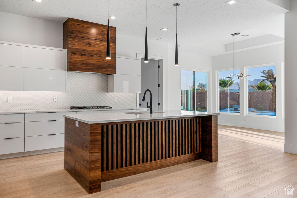 Kitchen featuring decorative light fixtures, backsplash, light hardwood / wood-style floors, a kitchen island with sink, and sink