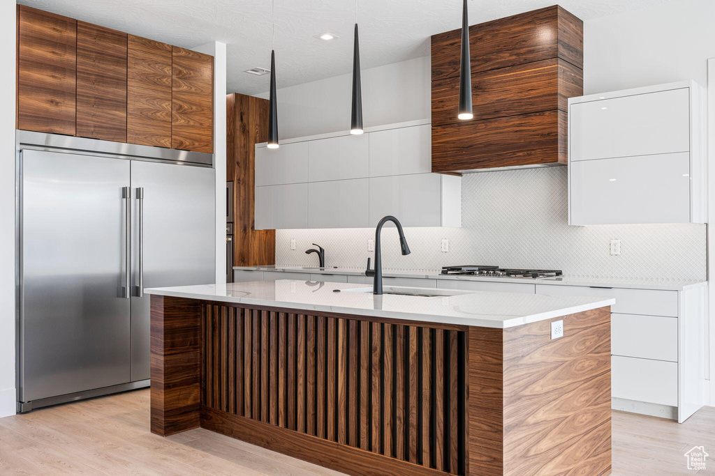 Kitchen featuring stainless steel built in fridge, light hardwood / wood-style flooring, backsplash, and a kitchen island with sink