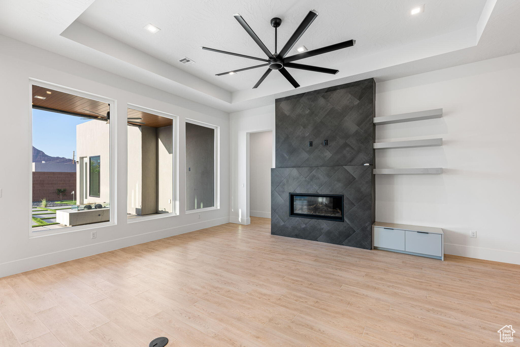Unfurnished living room featuring light hardwood / wood-style floors, ceiling fan, a fireplace, and a tray ceiling