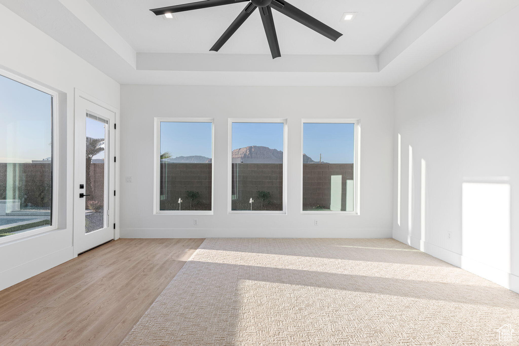 Empty room featuring plenty of natural light, ceiling fan, light hardwood / wood-style flooring, and a tray ceiling