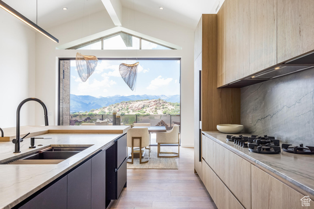 Kitchen featuring light wood-type flooring, a mountain view, light stone counters, sink, and vaulted ceiling