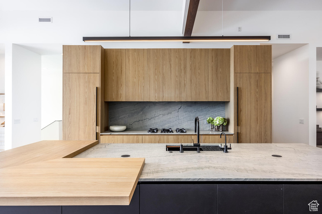 Kitchen with backsplash, light stone counters, sink, white gas stovetop, and beam ceiling