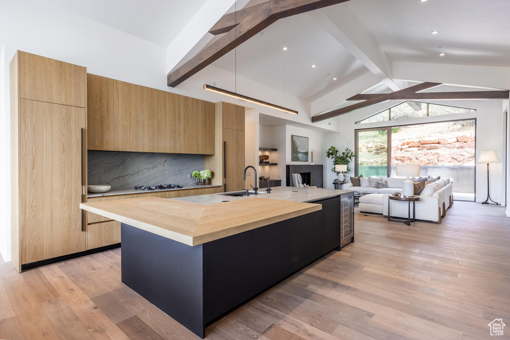 Kitchen featuring a center island with sink, butcher block counters, light wood-type flooring, and lofted ceiling with beams