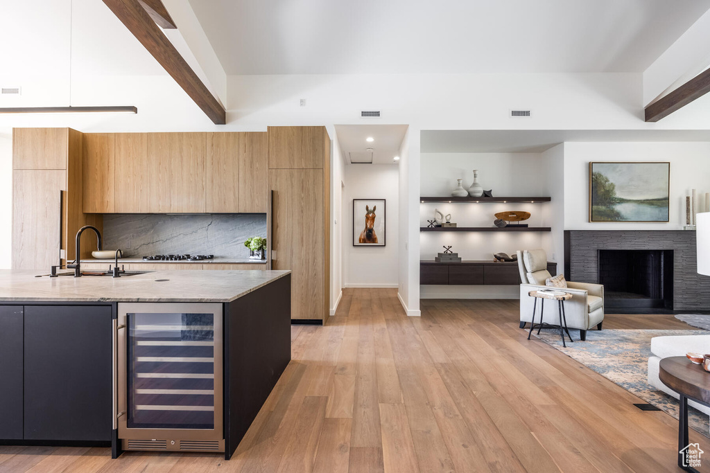 Kitchen with light wood-type flooring, beverage cooler, light stone counters, and beam ceiling