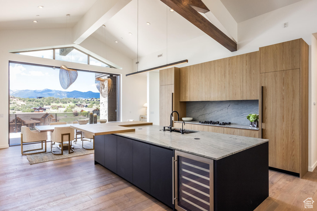 Kitchen with a mountain view, a center island with sink, beverage cooler, light hardwood / wood-style floors, and vaulted ceiling with beams