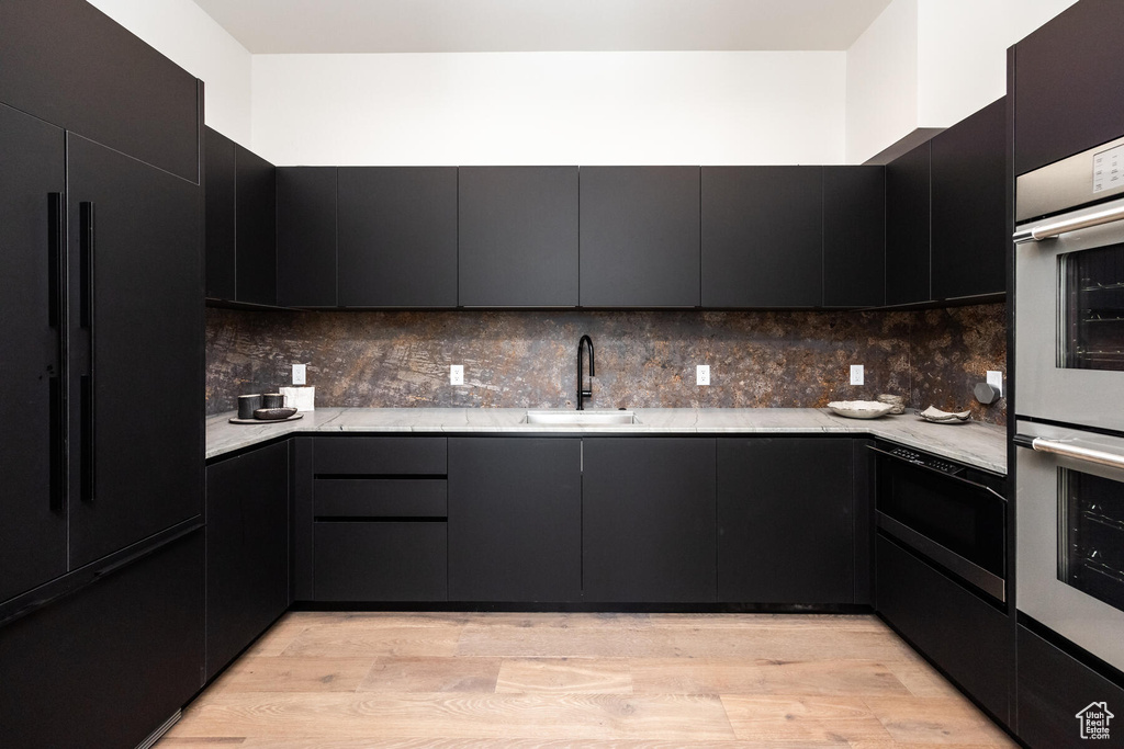 Kitchen featuring stainless steel double oven, light wood-type flooring, high end black refrigerator, sink, and tasteful backsplash