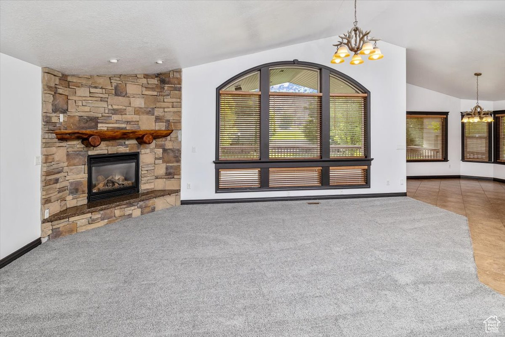 Unfurnished living room with tile floors, a notable chandelier, vaulted ceiling, and a stone fireplace