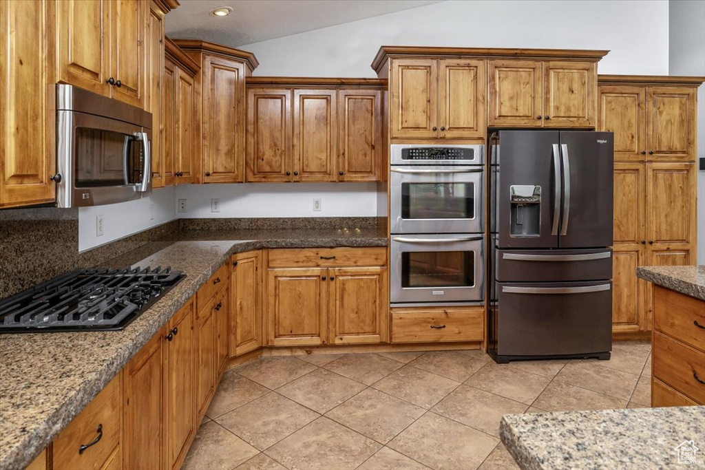 Kitchen featuring vaulted ceiling, stone counters, tasteful backsplash, appliances with stainless steel finishes, and light tile floors