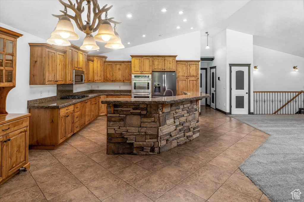 Kitchen with an island with sink, a notable chandelier, light tile floors, hanging light fixtures, and appliances with stainless steel finishes