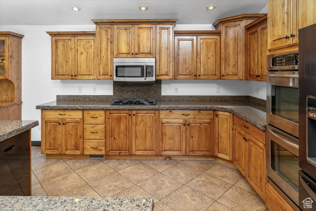 Kitchen featuring dark stone countertops, light tile flooring, and appliances with stainless steel finishes