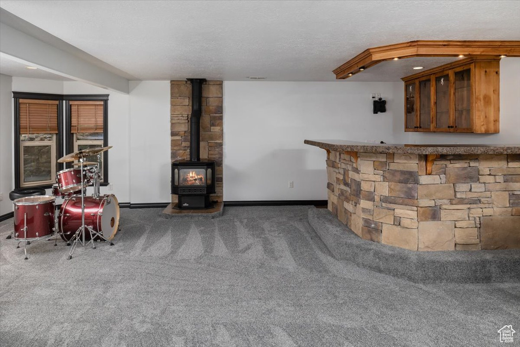 Unfurnished living room featuring a wood stove, a textured ceiling, and carpet floors