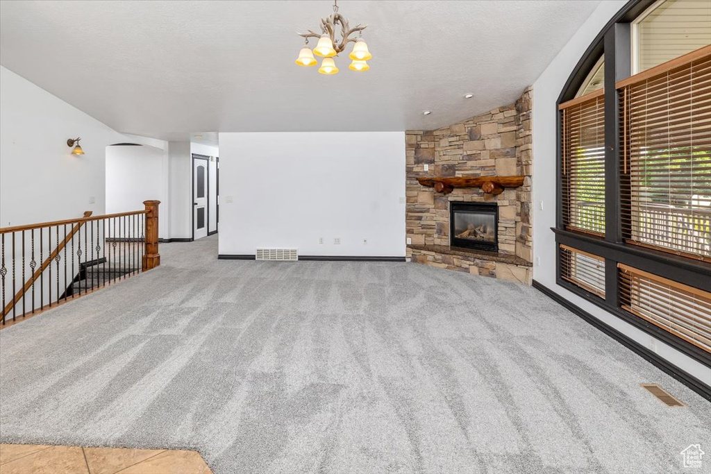 Unfurnished living room with a stone fireplace, an inviting chandelier, carpet flooring, and vaulted ceiling