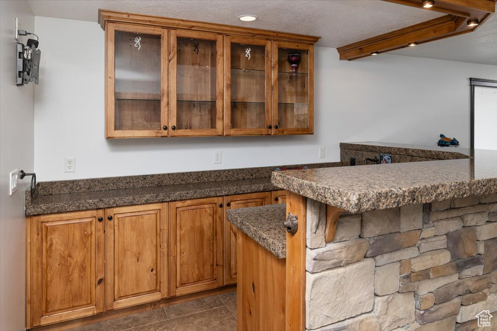 Kitchen featuring dark stone countertops, a textured ceiling, dark tile flooring, and kitchen peninsula