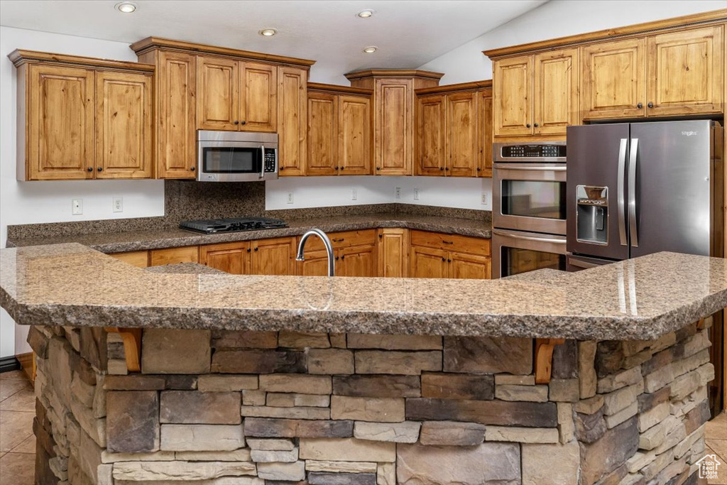 Kitchen featuring stainless steel appliances, vaulted ceiling, a breakfast bar area, and light tile floors