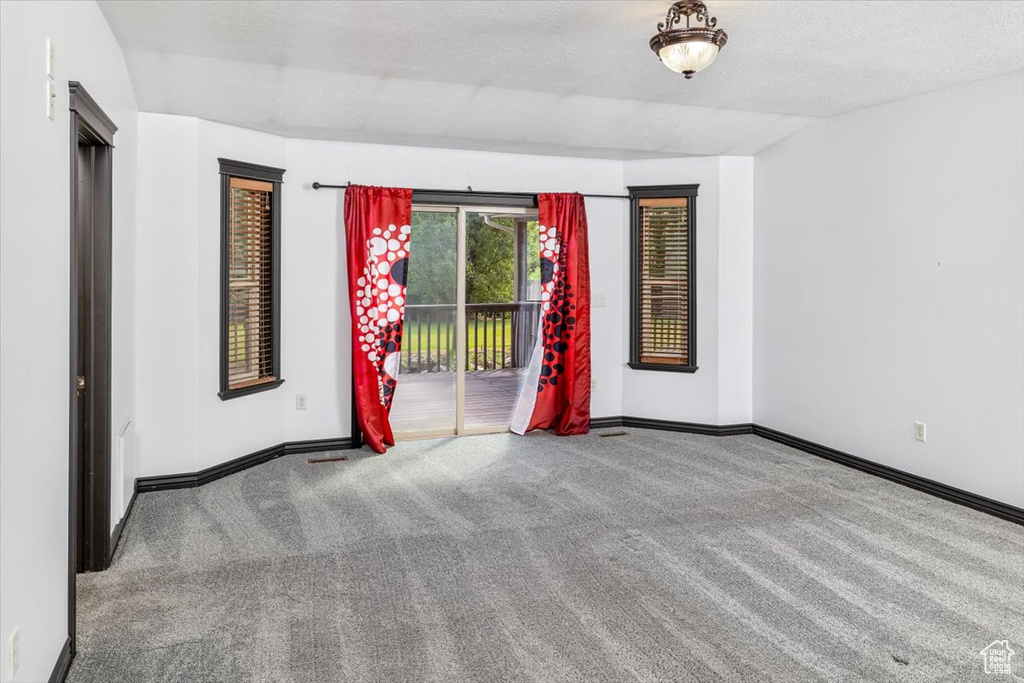 Carpeted empty room with a textured ceiling and vaulted ceiling