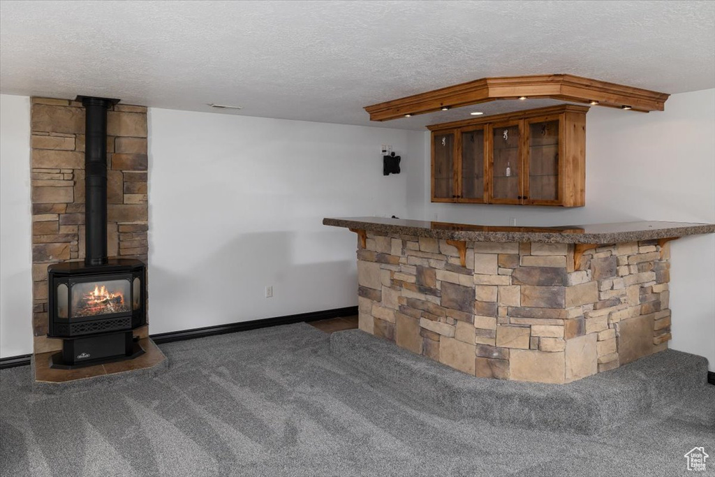 Bar featuring a textured ceiling, a wood stove, and dark colored carpet