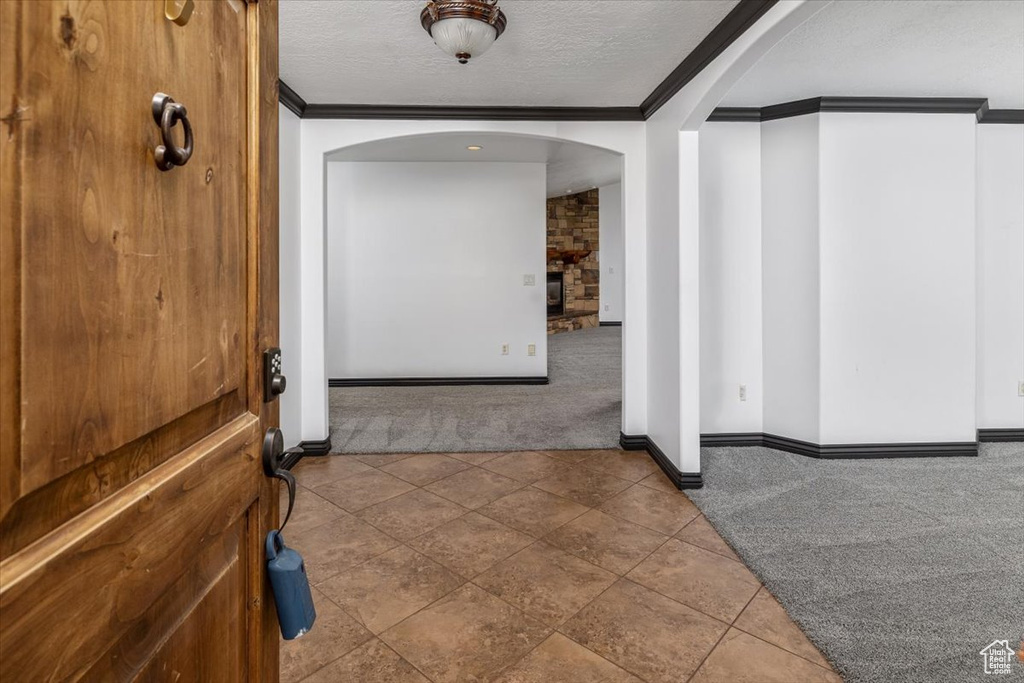 Corridor with a textured ceiling, ornamental molding, carpet, and brick wall