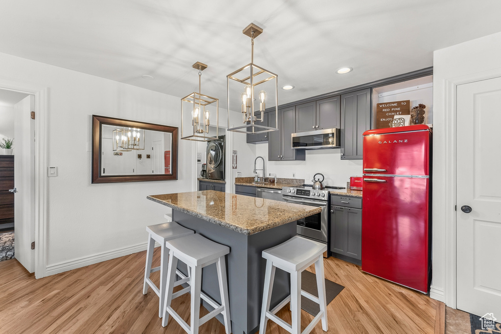 Kitchen featuring hanging light fixtures, light hardwood / wood-style flooring, a kitchen bar, and stainless steel appliances