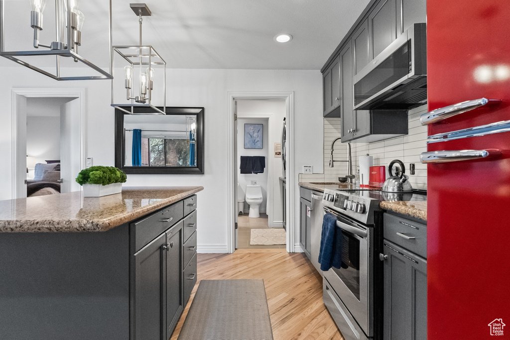 Kitchen featuring light hardwood / wood-style flooring, stainless steel appliances, pendant lighting, backsplash, and stone countertops