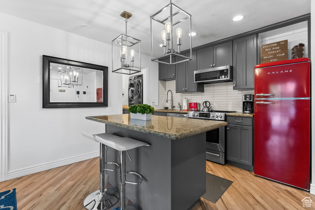 Kitchen with dark stone counters, light hardwood / wood-style floors, tasteful backsplash, washer / dryer, and appliances with stainless steel finishes