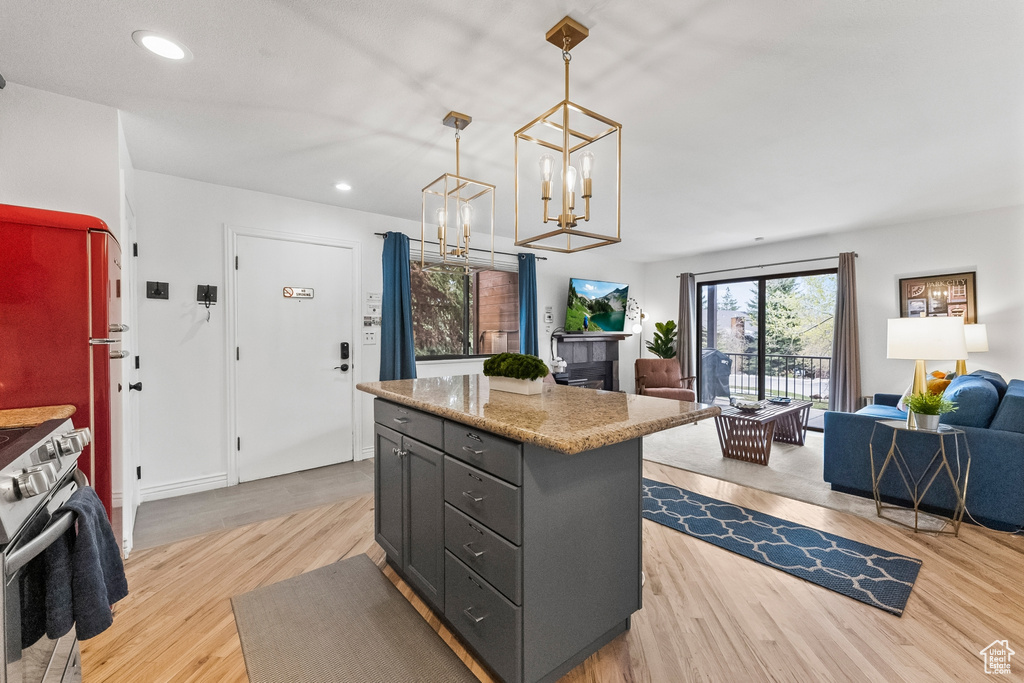 Kitchen with a center island, hanging light fixtures, light hardwood / wood-style flooring, light stone counters, and stainless steel range with electric stovetop