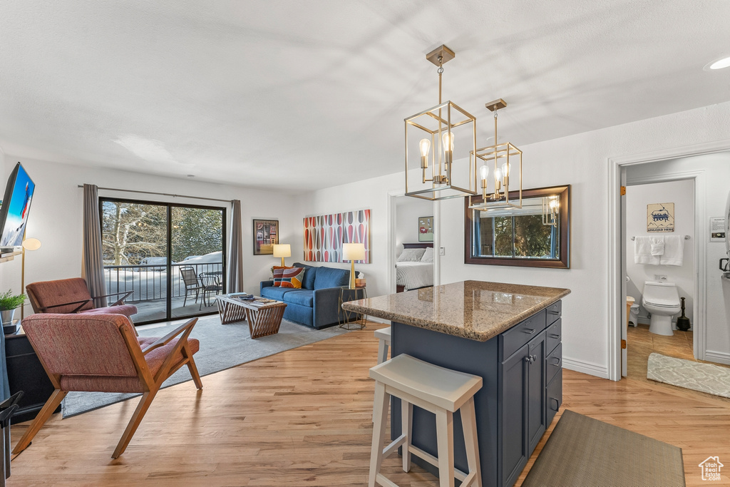 Kitchen with light hardwood / wood-style flooring, decorative light fixtures, an inviting chandelier, a center island, and stone countertops