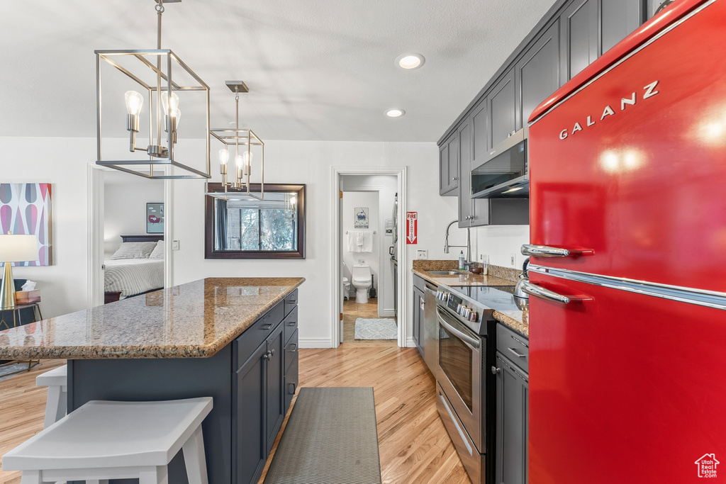 Kitchen with range hood, stainless steel range with electric stovetop, light wood-type flooring, and fridge