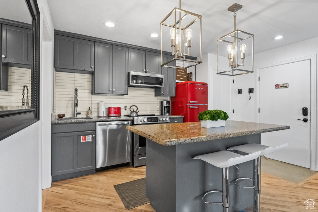 Kitchen featuring light hardwood / wood-style floors, backsplash, a kitchen bar, appliances with stainless steel finishes, and sink