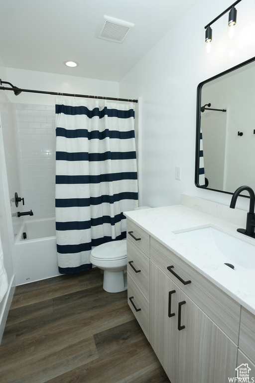 Full bathroom featuring shower / bath combo with shower curtain, toilet, vanity, and hardwood / wood-style floors