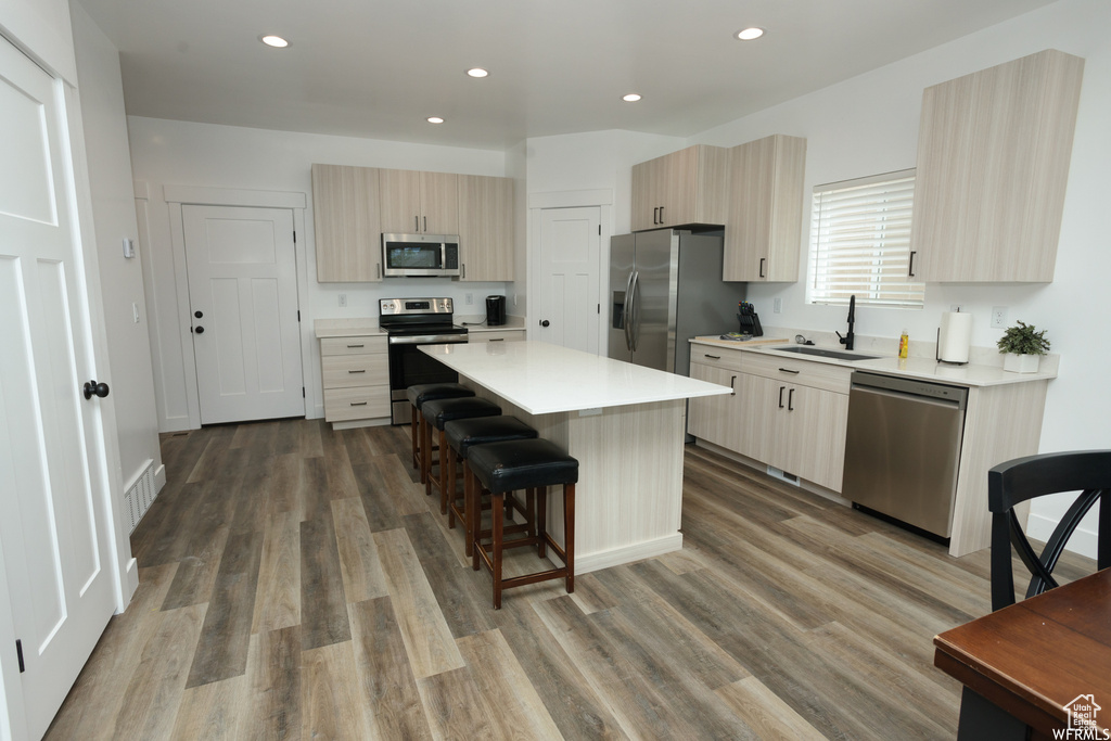 Kitchen with a kitchen island, appliances with stainless steel finishes, wood-type flooring, and sink