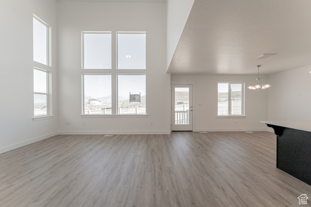 Unfurnished living room with light wood-type flooring, a high ceiling, and a notable chandelier