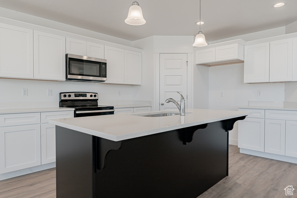 Kitchen featuring decorative light fixtures, white cabinets, appliances with stainless steel finishes, and an island with sink