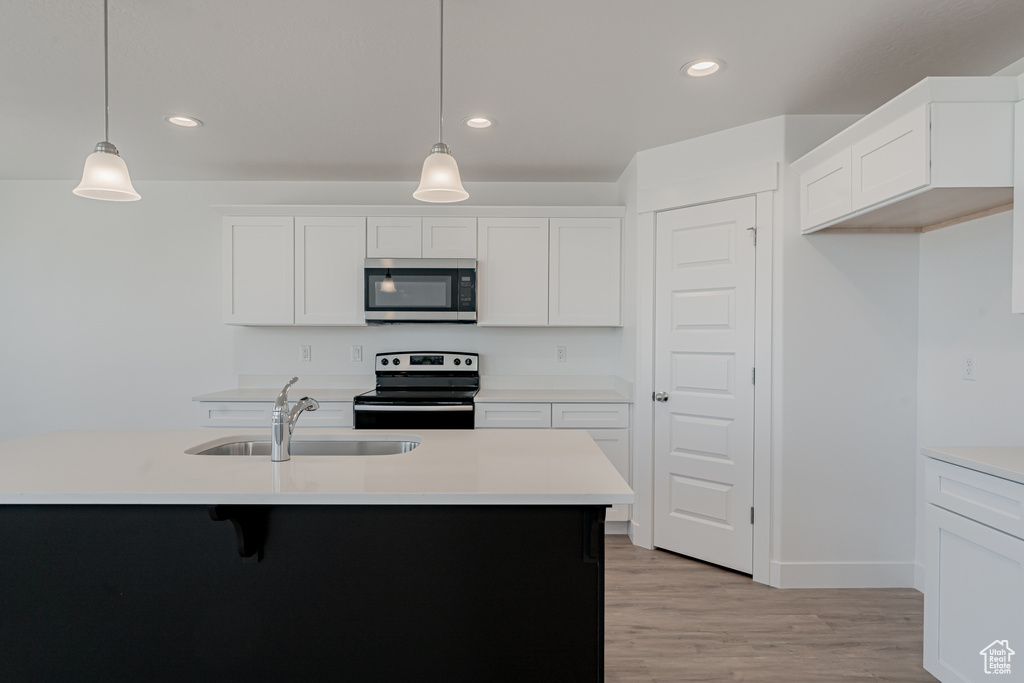 Kitchen with white cabinets, light hardwood / wood-style flooring, decorative light fixtures, appliances with stainless steel finishes, and sink