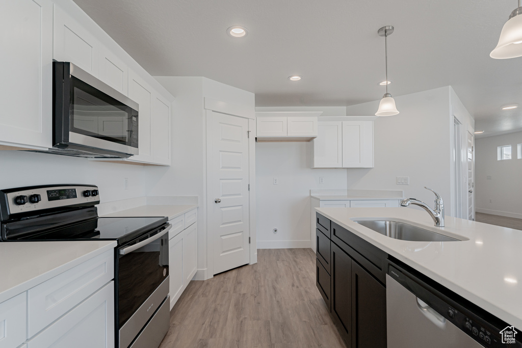 Kitchen featuring hanging light fixtures, sink, appliances with stainless steel finishes, and white cabinetry