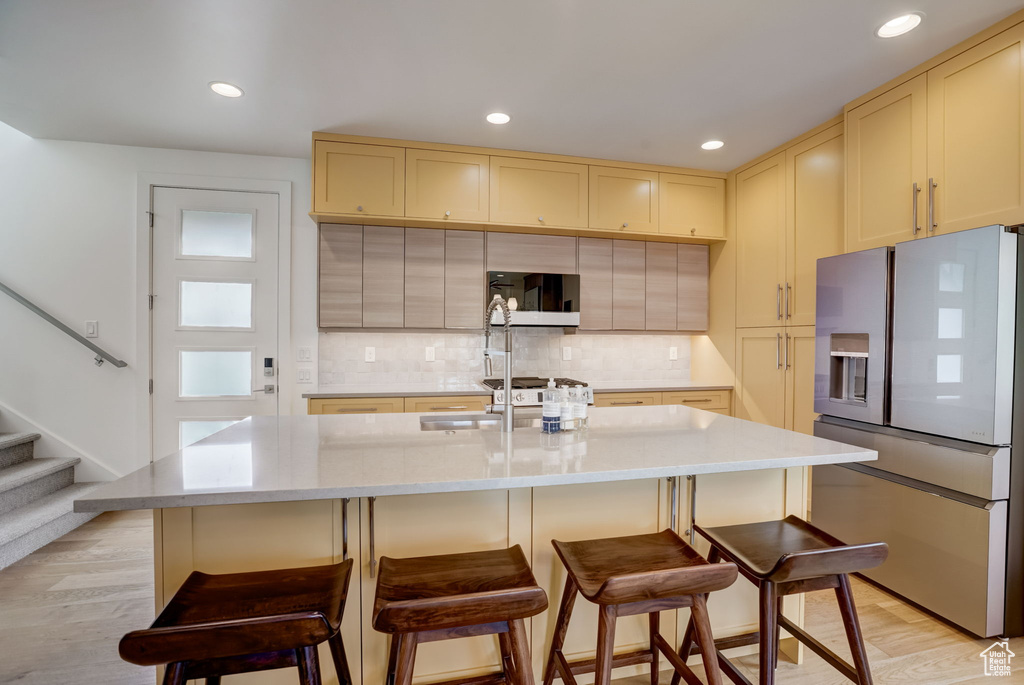 Kitchen featuring light wood-type flooring, a kitchen island with sink, and stainless steel refrigerator with ice dispenser