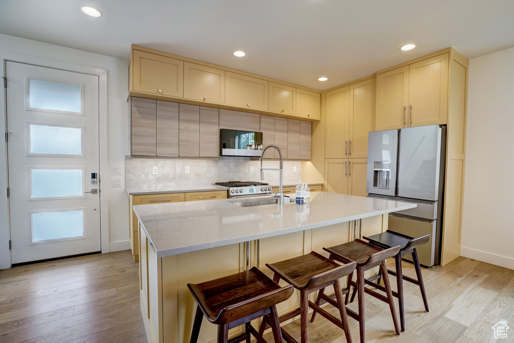 Kitchen featuring a kitchen breakfast bar, a kitchen island with sink, stainless steel refrigerator with ice dispenser, light wood-type flooring, and tasteful backsplash