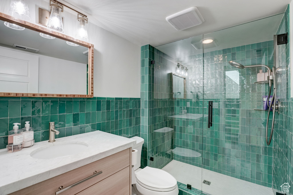 Bathroom with backsplash, a shower with door, tile walls, and large vanity