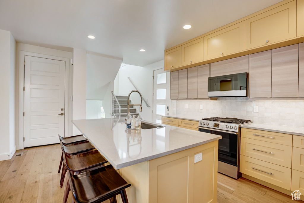 Kitchen featuring backsplash, light hardwood / wood-style flooring, a breakfast bar area, a center island with sink, and stainless steel range with gas cooktop