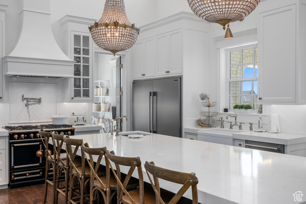 Kitchen with custom exhaust hood, premium appliances, tasteful backsplash, dark hardwood / wood-style flooring, and pendant lighting