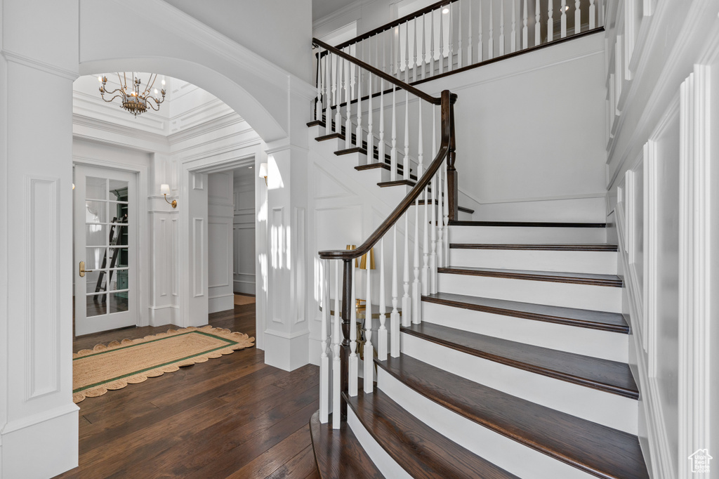 Staircase with dark hardwood / wood-style flooring, a high ceiling, crown molding, and a chandelier