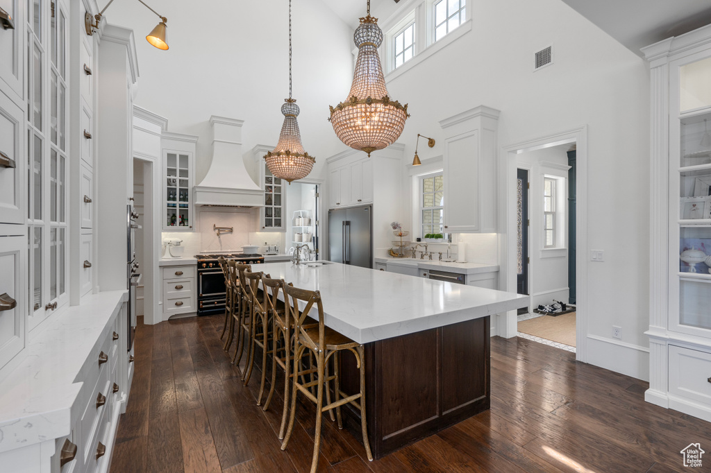 Kitchen with premium range hood, dark wood-type flooring, high end appliances, and a kitchen island with sink